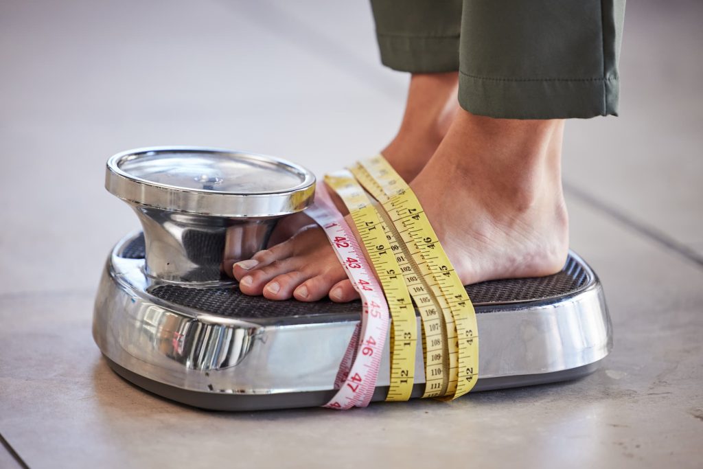 why am i not losing weight on semaglutide? woman standing on scale with measuring tape wrapped around the scale